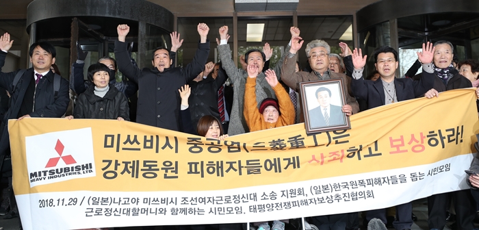 Las víctimas coreanas del trabajo forzado durante la Segunda Guerra Mundial y sus familiares levantan la mano después de ganar una demanda contra la compañía japonesa, Mitsubishi Heavy Industries Ltd., con una indemnización frente a la Corte Suprema en Seocho-gu, Seúl, 29 de noviembre. | Yonhap News