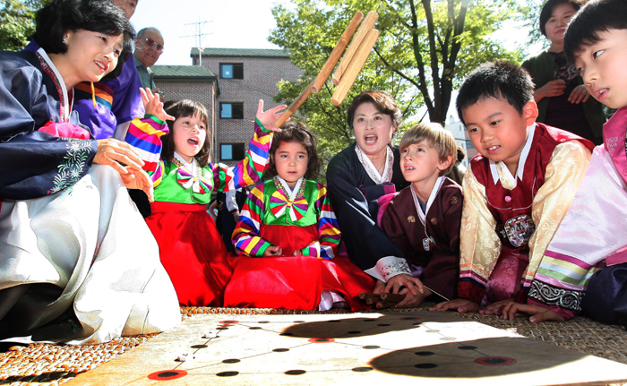 En Seollal, un grupo de niños vestidos con hanbok juegan un juego tradicional de mesa en el que se usan cuatro barras de madera y se conoce como yunnori