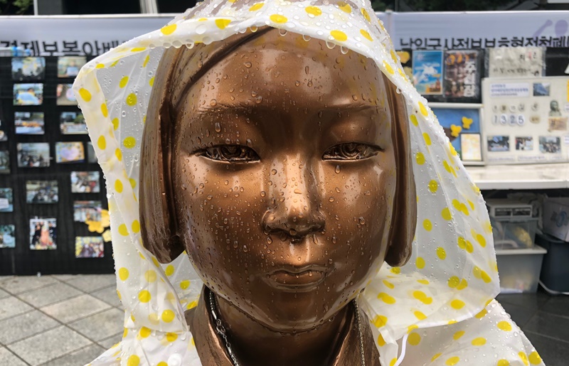 El destino final de los manifestantes fue la "Estatua de la paz", una pieza de bronce con forma de una niña que presenta a las mujeres de consuelo forzadas a servir como esclavas sexulaes por Japón durante tiempos de guerra. Los asistentes coreanos y japoneses de la marcha pusieron un impermeable sobre la estatua. En medio de una mayor tensión entre Corea y Japón sobre cuestiones históricas, es difícil decir si las gotas en la cara de la estatua son lluvia o lágrimas. | Kim Minji
