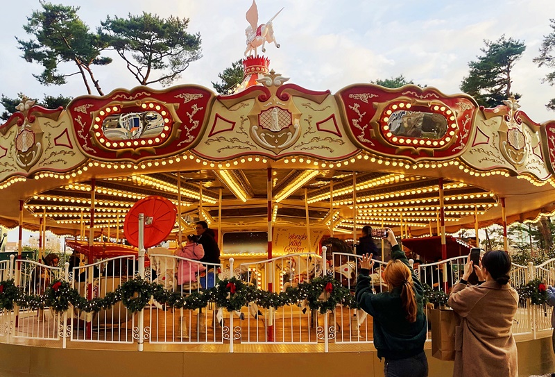 La torre Lotte World, en el distrito Songpa-gu de Seúl, alberga el fantástico Jardín de los Deseos al aire libre. Después de atravesar la puerta del jardín laberíntico que marca el inicio del complejo, los visitantes son recibidos por un gran árbol de Navidad de 19 metros de altura, decorado con ornamentos y luces de colores, con un tiovivo detrás. | Lee Dasom