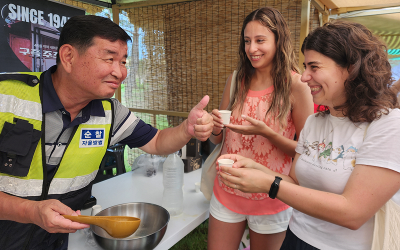  El 27 de julio, Vivian Souza de Brasil (primera desde la derecha) y su amiga boliviana María Fernanda Paniagua (centro) prueban makgeolli de durazno en el puesto de bebidas. Cuando la periodista de Korea.net les preguntó su opinión sobre esta bebida, Souza respondió diciendo que 