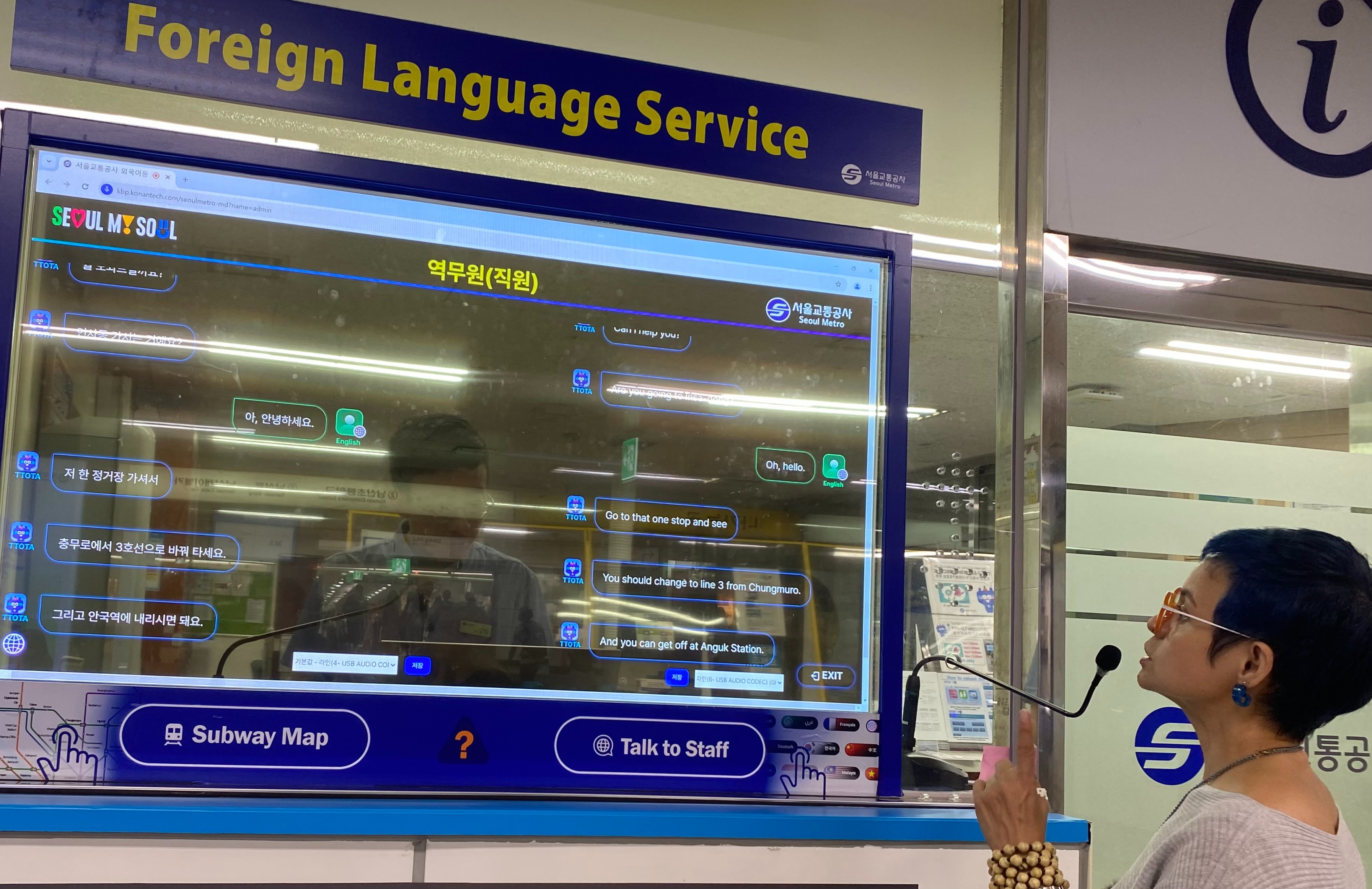 El 22 de agosto, la reportera honoraria Mae Young utiliza el servicio de interpretación simultánea basado en inteligencia artificial (IA) en la estación Myeongdong, en Seúl. Una vez que un miembro del personal y un pasajero hablan, el sistema muestra automáticamente el texto traducido en una pantalla transparente que divide la oficina del metro de los usuarios. El servicio se ofrece en 13 idiomas en las 11 estaciones del metro de Seúl más frecuentadas por los turistas extranjeros, incluidas las estaciones de Gwanghwamun, Hongik University y Gimpo International Airport. | Mae Young