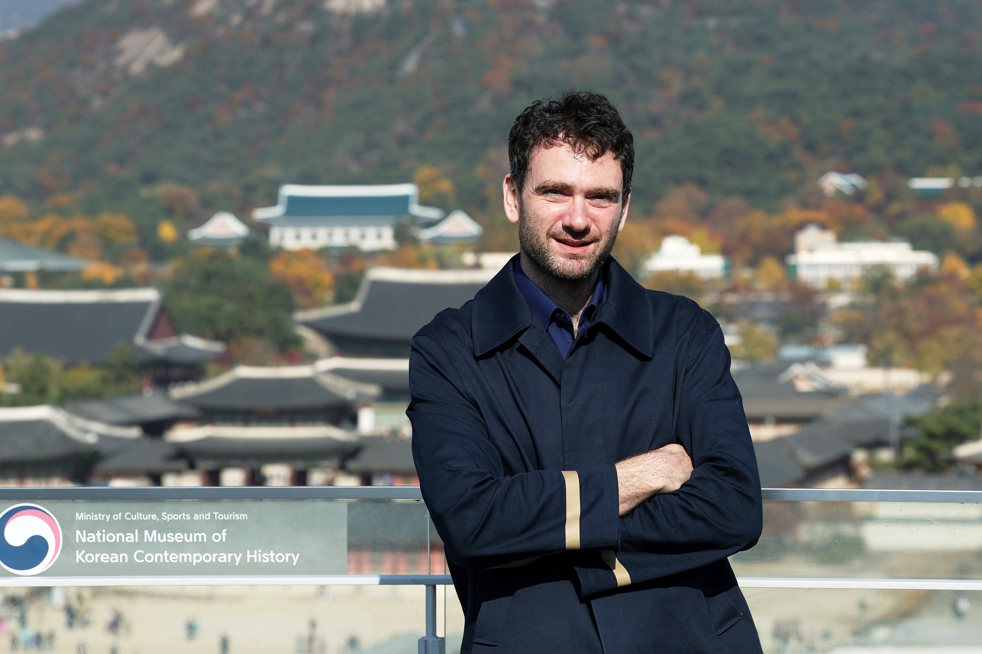 Daniel Tudor, autor británico afincado en Seúl que ha escrito varios libros de no ficción sobre Corea, posa para una foto el 13 de noviembre en el tejado del Museo Nacional de Historia Contemporánea de Corea, en Seúl, con el palacio de Gyeongbokgung al fondo. | Lee Jun Young