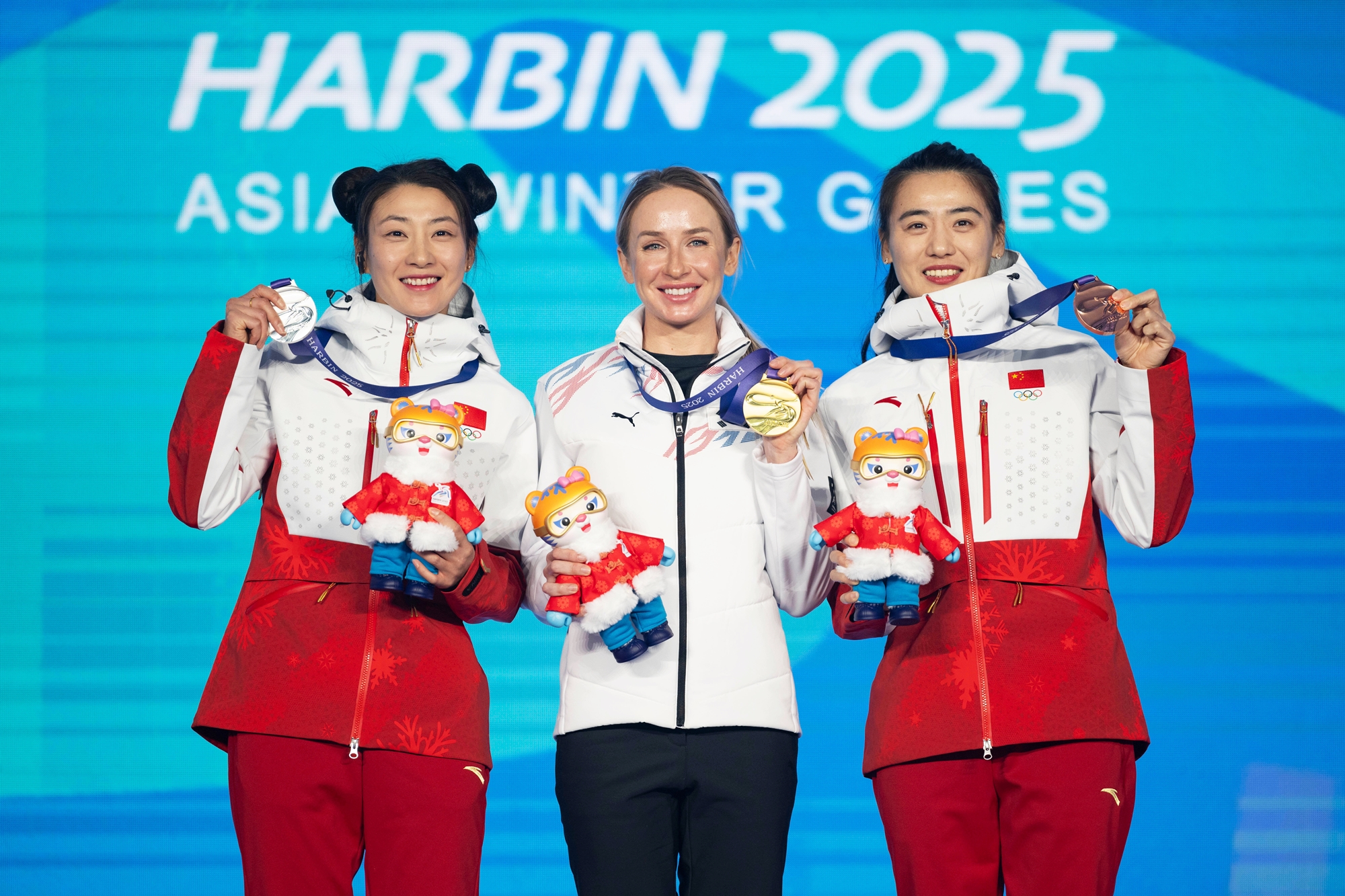 Ekaterina Avvakumova (centro), una atleta naturalizada coreana, originaria de Rusia, posa el 11 de febrero con su medalla de oro del esprint de 7,5 kilómetros de biatlón femenino de los Juegos Asiáticos de Invierno, en la Estación de Esquí de Yabuli, a unos 200 kilómetros al sudeste de la principal ciudad anfitriona, Harbin. La atleta quedó en el primer puesto, con un tiempo récord de 22 min 45 s 4 cs.  