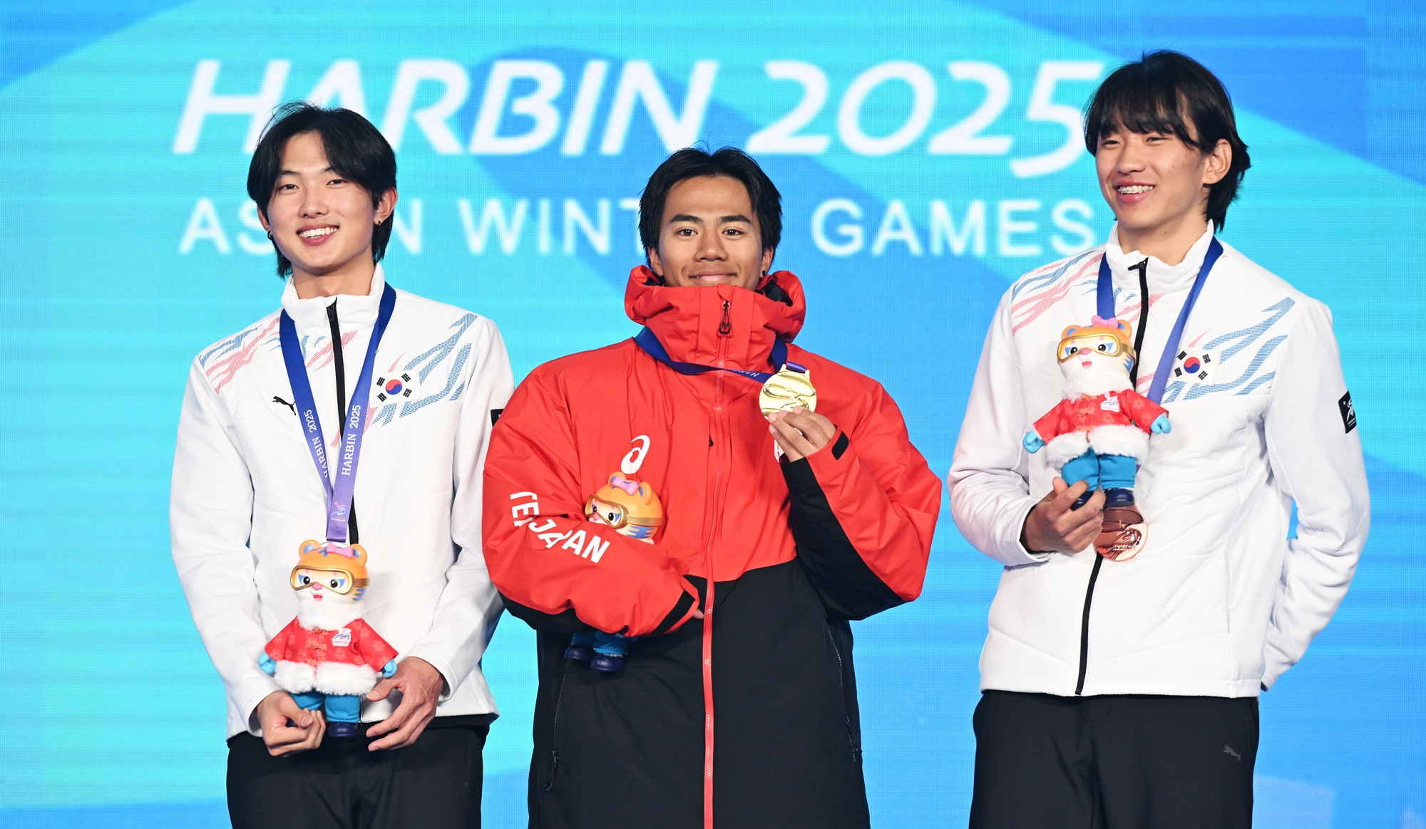 Yoon Jonghyun (izquierda) y Shin Yeongseop (derecha) posan con el japonés Rai Kasamura en el podio masculino de esquí de estilo libre en big air de los Juegos Asiáticos de Invierno de Harbin, en el Estadio de Freeski Big Air, el 12 de febrero. | Agencia de Noticias Yonhap