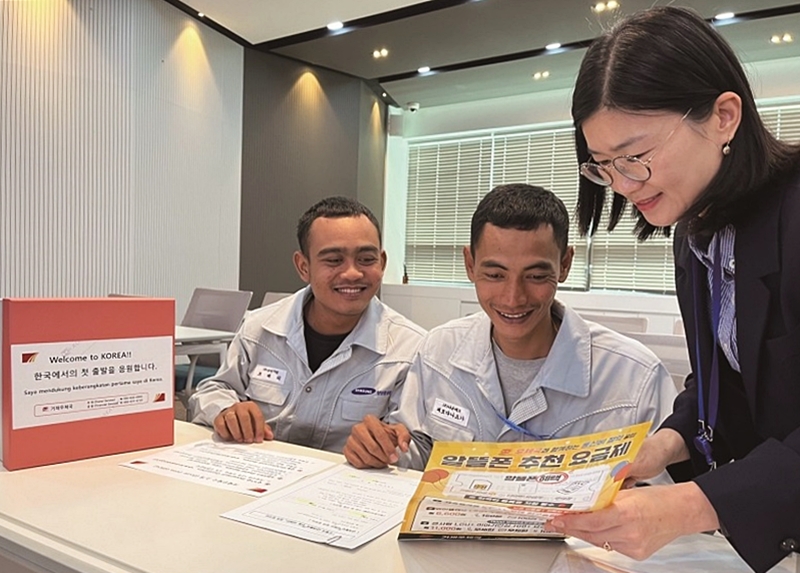 Dos extranjeros escuchan sobre los envíos de correos y los servicios financieros en una oficina de correos. | Korea Post