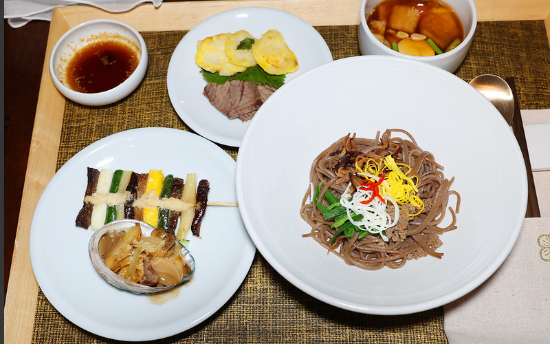 'Los platos servidos en 'La mesa del emperador' (en el sentido de las agujas del reloj, desde abajo a la derecha): goldongmyeon (fideos con guarniciones variadas), jeonbokcho (abalón hervido con salsa de soya), hwayangjeok (brochetas de colores), chojang (salsa de vinagre con soya), jeonyueo (pescado blanco frito), pyeonyuk (falda de res cocida y fileteada) y jang kimchi (kimchi de agua sazonado con salsa de soya).