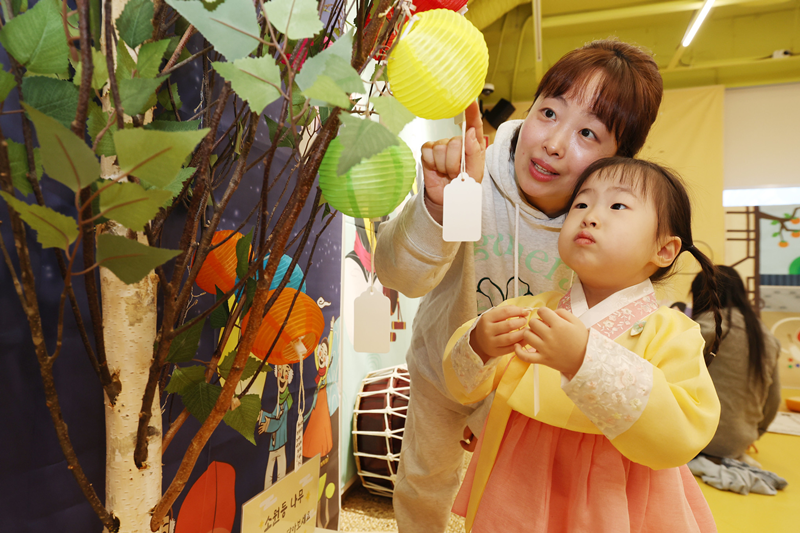 El 12 de febrero, en vísperas del Año Nuevo Lunar, una madre y su hija comparten un momento de unión frente al árbol de los deseos en la sección de juegos tradicionales de un café infantil en el distrito de Gangdong-gu, en Seúl, reflejando la conexión que los juegos tradicionales crean entre las familias.style=
