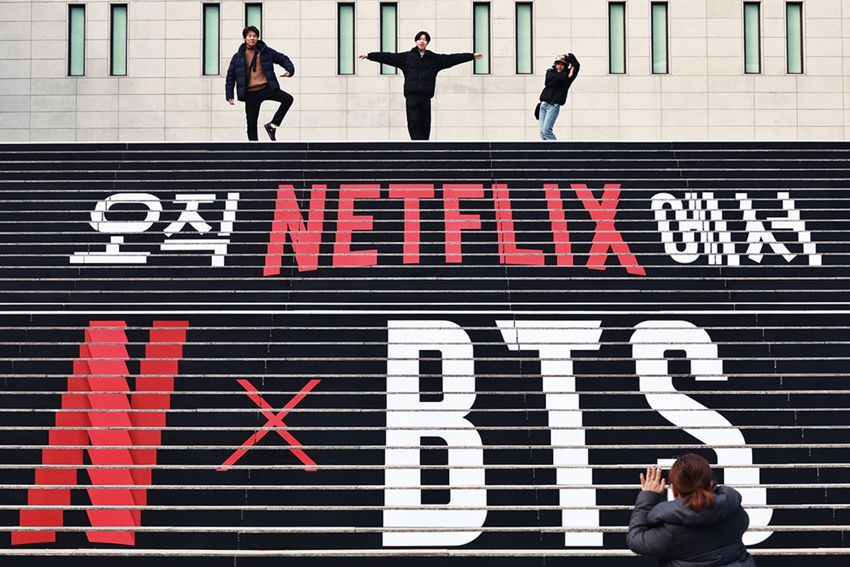 La foto, tomada el 11 de marzo, muestra a unos turistas extranjeros tomándosen una fotografía frente a los carteles promocionales del concierto de BTS, en las escaleras del Centro Sejong para las Artes Escénicas, en el distrito de Jongno-gu, en Seúl. | Agencia de Noticias Yonhap