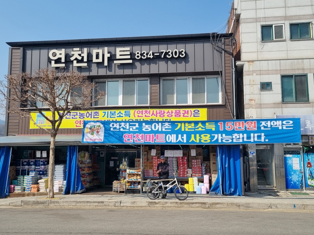 En la foto, tomada el 17 de marzo, se observa una pancarta colgada en la entrada de un supermercado del condado de Yeoncheon-gun, en la provincia de Gyeonggi-do. En ella se informa a los residentes que pueden utilizar la totalidad de su bono de renta básica rural en los establecimientos comerciales de la zona. | Aisylu Akhmetzianova