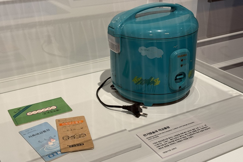 La foto muestra una arrocera eléctrica y una libreta de ahorros, dos de los regalos más comunes que las empresas otorgaban a los recién casados durante el período de rápida industrialización en Corea.