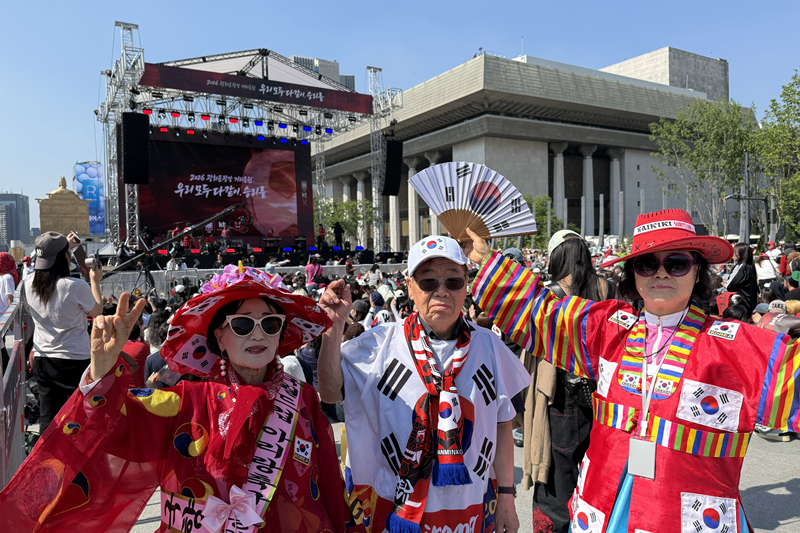 Los miembros del grupo de animación de Arirang, vestidos con trajes tradicionales coreanos, apoyan a la selección nacional antes del partido entre Corea y la República Checa, trasmitido en vivo en pantallas gigantes en la plaza de Gwanghwamun, en el distrito de Jongno-gu, Seúl. | Angie Hong