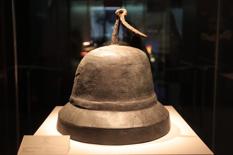En la imagen se aprecia la Gran campanilla de viento de bronce descubierta en el sitio del pabellón Bogwangjeon, en las ruinas del templo Hoeamsa. La pieza tiene grabados 134 caracteres que incluyen los nombres del rey Taejo, la reina Sindeok, el príncipe heredero Bangseok y el monje Muhak, lo que demuestra la relevancia de este templo durante los primeros años de la dinastía Joseon. style=