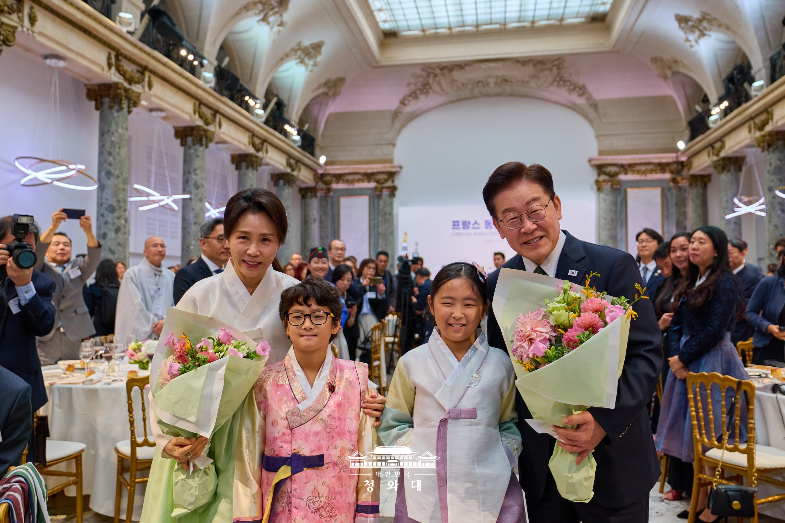 El presidente Lee Jae Myung (derecha) y la primera dama, Kim Hea Kyung, sostienen ramos de flores entregados por ni&ntilde;os, durante un almuerzo con la comunidad de coreanos resididos en Francia, celebrado el 9 de septiembre en el hist&oacute;rico recinto Pavillon Cambon Capucines, en Par&iacute;s, en Francia.