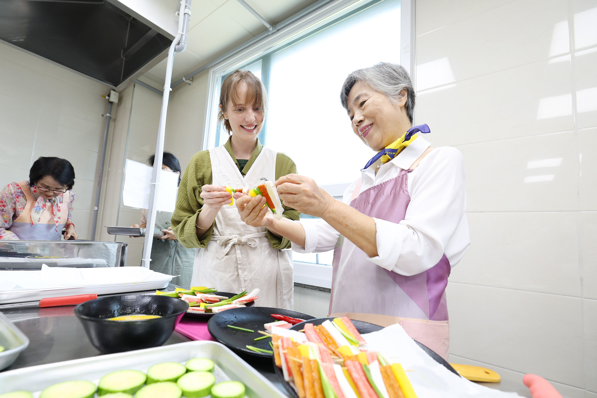 Una persona mayor ense&ntilde;a a una extranjera a preparar platos festivos tradicionales durante una clase culinaria internacional de Chuseok, celebrada el 30 de septiembre de 2025, en el Centro de Bienestar para Personas Mayores de Yongsan, en el distrito de Yongsan-gu, en Se&uacute;l. | Korea.net DB 