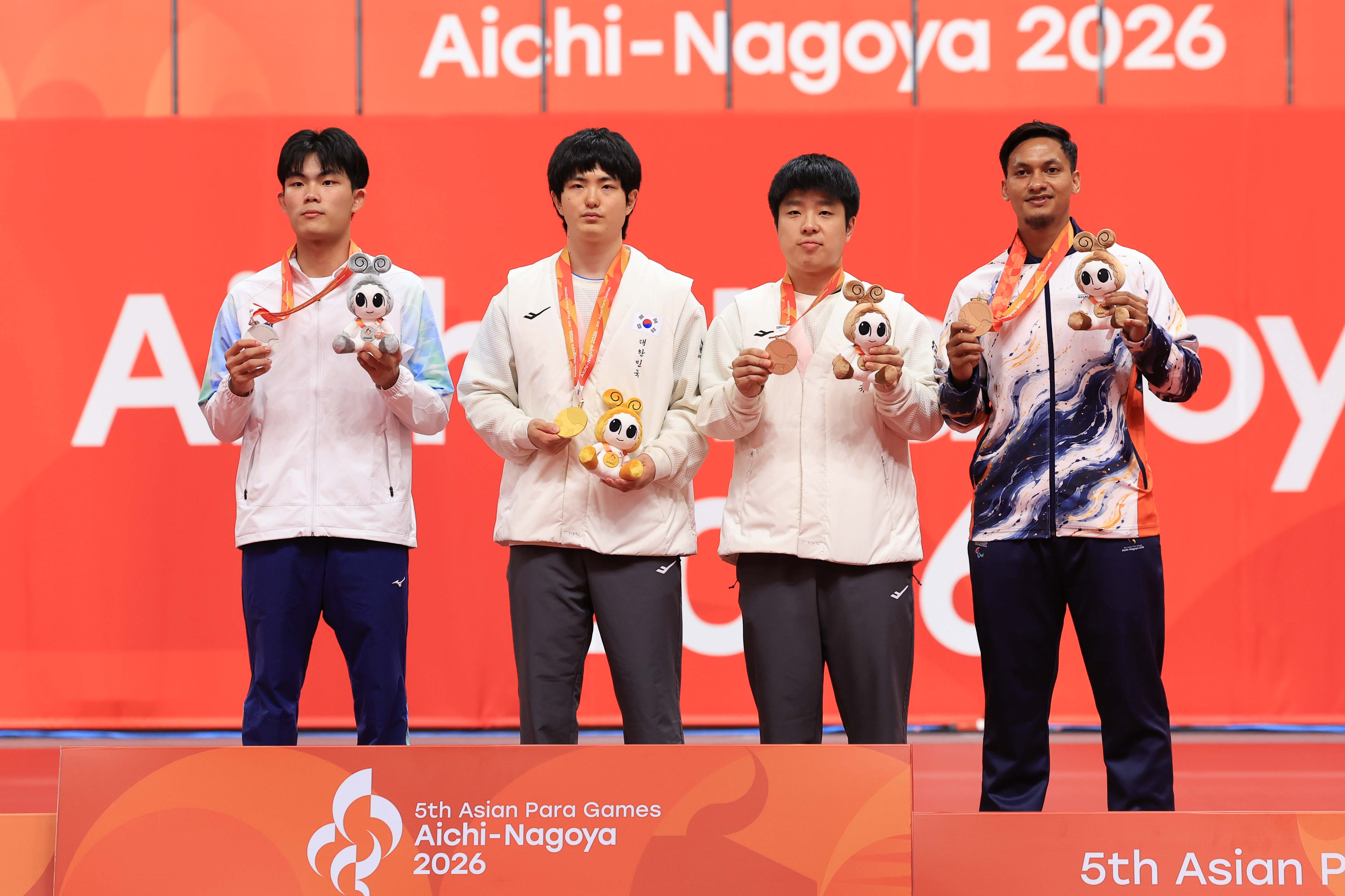 Los coreanos Kim Gitae (segundo desde la izquierda) y Kim Bogyeom (tercero desde la izquierda), quienes se adjudicaron el oro y el bronce en tenis de mesa en la categoría individual masculina de clase 11 en los Juegos Para Asiáticos de Aichi-Nagoya 2026, sostienen sus medallas durante la ceremonia de premiación el 20 de octubre en el pabellón Sky Hall Toyota, en la prefectura de Aichi, Japón.
