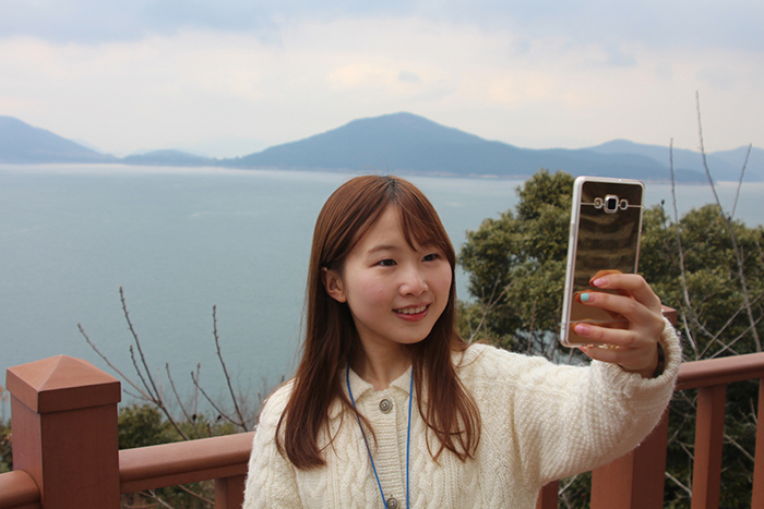 A tourist takes a picture with the sea in the background at Jangsado.