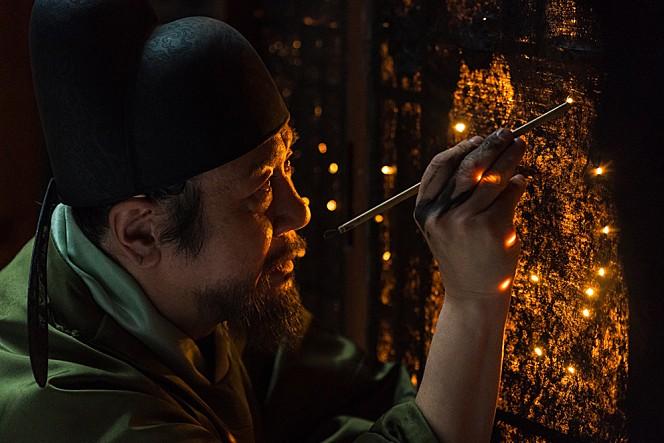 Yeong-Sil cubre con pintura negra los paneles de papel de las paredes del cuarto real y va creando las constelaciones, haciendo pequeñas perforaciones que se iluminan con la luz de la vela del chambelán que se encuentra al otro lado de la pared. l Lotte Entertainment