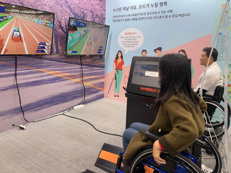 En la foto, se muestran dos visitantes jugando a un juego de realidad aumentada (RA) de carreras en silla de ruedas.