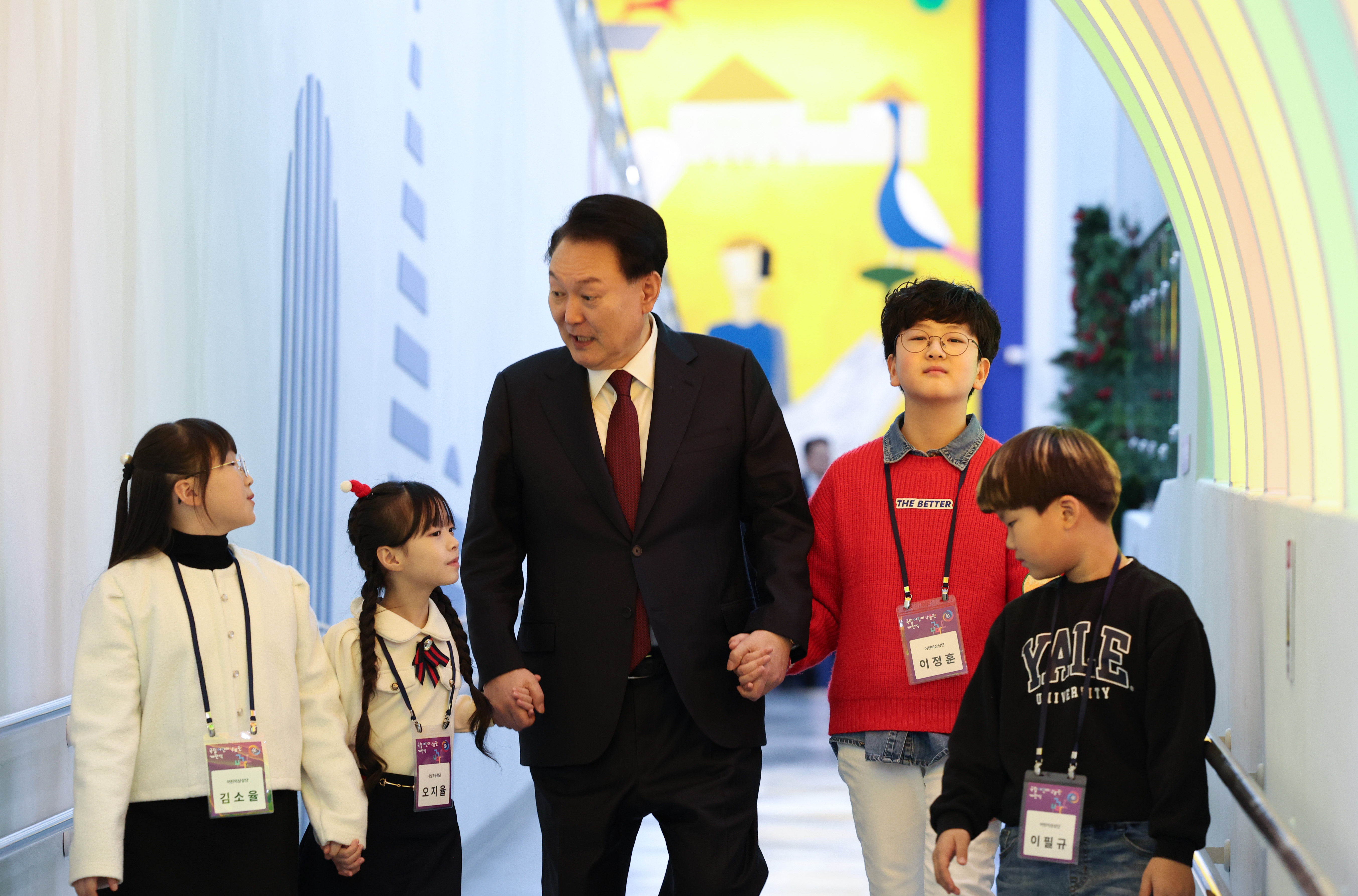 El 16 de diciembre de 2023, el presidente Yoon camina junto con unos niños mientras recorre la sala de exposiciones del Museo Nacional de los Niños durante la ceremonia de apertura de este último en el Complejo del Museo Nacional de Corea en la ciudad de Sejong. Para abordar la baja tasa de natalidad, su Administración abolió los criterios de ingresos máximos para apoyar el tratamiento de infertilidad y aumentó los beneficios parentales de 700.000 wones a 1 millón de wones por recién nacido. 