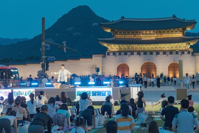 El 21 de junio, un instructor de yoga enseña una postura a los participantes del evento 'Gwanghwamun Moonlight Yoga' en el Yukjo Madang de la plaza Gwanghwamun, en el distrito Jongno-gu de Seúl. | Gobierno Metropolitano de Seúl