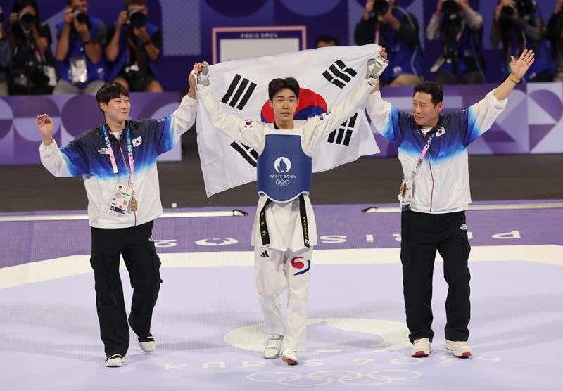 El 7 de agosto (hora local), el taekwondista coreano Park Tae Joon (centro) levanta la bandera surcoreana en el Gran Palacio de París, luego de ser nombrado como el ganador de la prueba masculina de taekwondo de 58 kilogramos en los Juegos Olímpicos de París.