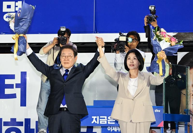 En la madrugada del 4 de junio, el candidato presidencial Lee Jaemyung y su esposa Kim Hyekyung levantan los brazos en señal de victoria con un ramo de flores, tras confirmarse su triunfo en las elecciones del día anterior. La celebración tuvo lugar durante un evento de seguimiento del escrutinio organizado por el Partido Democrático de Corea, cerca de la Asamblea Nacional en el distrito Yeongdeungpo-gu de Seúl.