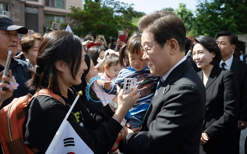 El presidente Lee Jae-myung (derecha) es saludado por sus vecinos la mañana del 4 de junio, antes de salir de su residencia en un complejo de apartamentos en el distrito de Gyeyang-gu, Incheon, rumbo al Cementerio Nacional de Seúl. En todo el complejo se colgaron pancartas felicitándolo por su victoria electoral.