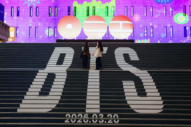 Dos fanes del grupo superestrella de K-pop BTS se detienen la noche del 6 de enero en la escalinata central del Centro Sejong para las Artes Esc&eacute;nicas, en el distrito de Jongno-gu, en Se&uacute;l, donde se exhiben instalaciones que promocionan el regreso del septeto este a&ntilde;o. 