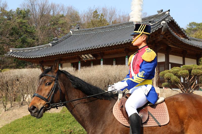 El cadete de tercer año, Jang won hyeok, pasa frente al Cheongheondang, el antiguo pabellón del Samgunbu, la máxima institución militar durante la dinastía Joseon. La unidad de caballería demuestra que la fuerza no reside solo en la rapidez o el ímpetu; el orden que se mantiene con absoluta templanza es, en sí mismo, un poder formidable.