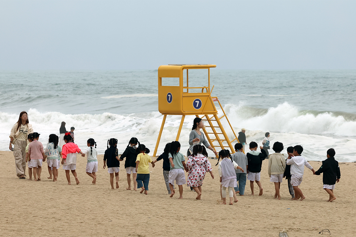 Unos ni&ntilde;os de guarder&iacute;a caminan por la arena siguiendo a su profesora, el 22 de junio, en la playa de Gyeongpo, en Gangneung, provincia de Gangwon-do.