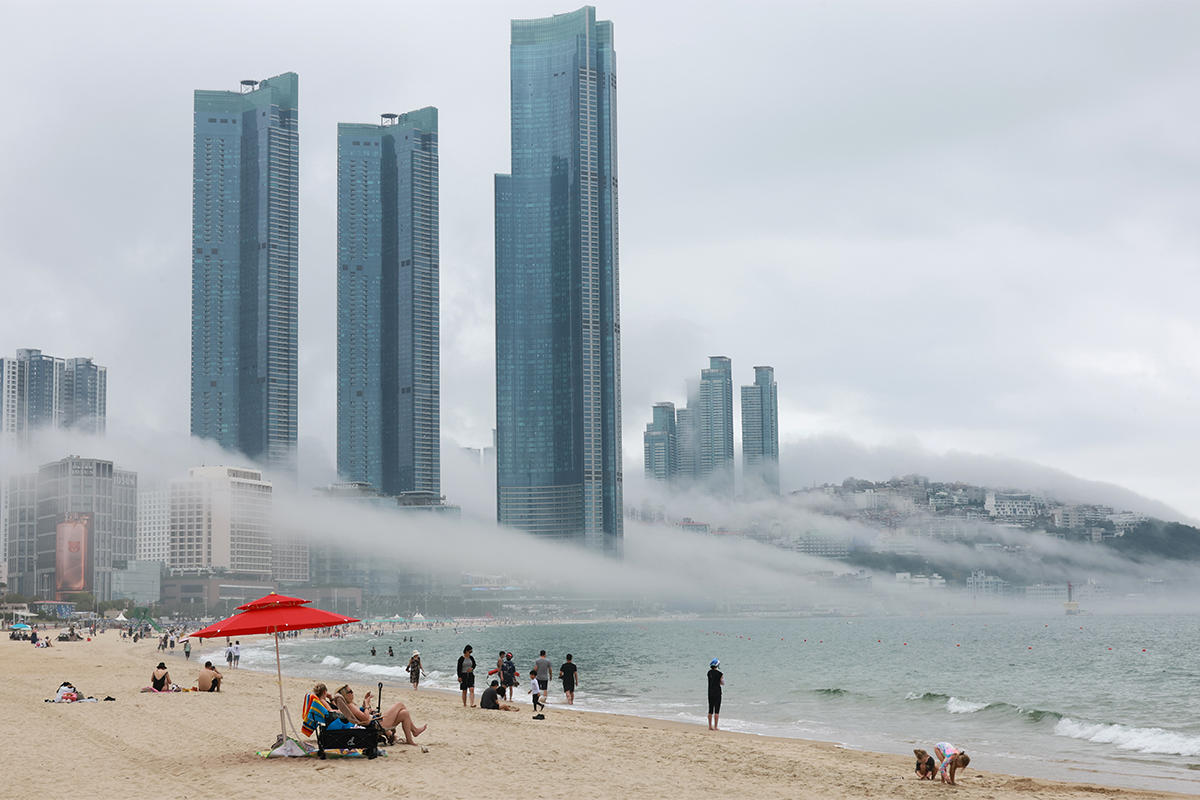El 7 de julio, ciudadanos y turistas disfrutan del mar y pasean por la orilla de la playa de Haeundae, en Busan, mientras una densa niebla marina que se extiende a lo largo de la costa.