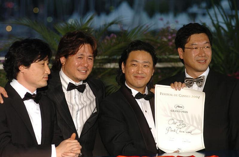 De izquierda a derecha, el CEO de Yong Film y productor Lim Seung-yong, el actor Choi Min-sik, el director Park Chan-wook y el director de fotografía Chung Chung-hoon posan juntos el 22 de mayo de 2004, tras ganar el Gran Premio del Jurado por 'Oldboy' en el Festival de Cine de Cannes, en el Pacio de Festivales y Congresos de Cannes, en Francia. | Biblioteca de medios del Festival de  Cannes