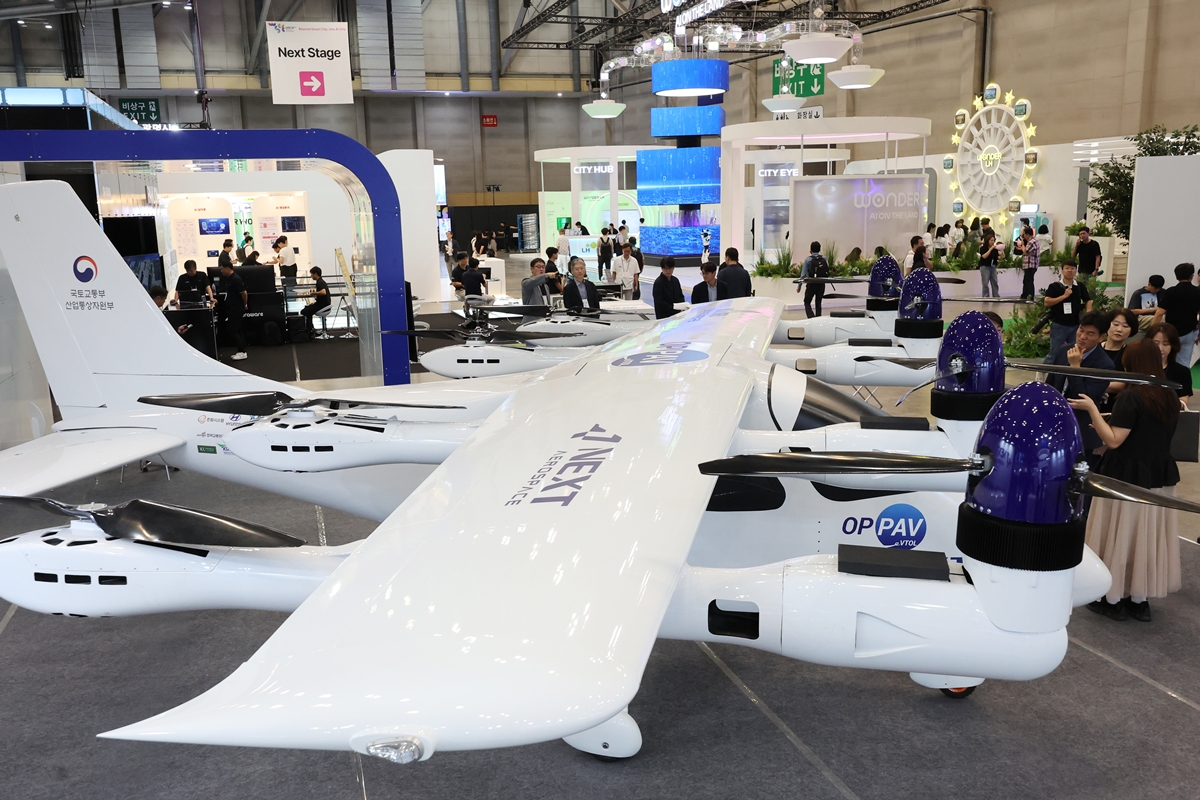 Los visitantes observan un dron de despegue y aterrizaje vertical (VTOL, por sus siglas en inglés) de alta maniobrabilidad y despliegue rápido, así como un prototipo de aeronave monoplaza VTOL con propulsión distribuida (opcionalmente tripulada), en la sala 1 de exposiciones del Centro de Exposiciones y Convenciones de Busan (BEXCO), en el distrito de Haeundae-gu de la citada ciudad, en el marco de la 