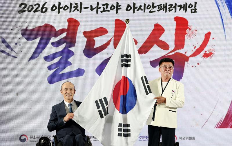 El lider de la delegación coreana, Park Heung-sik (derecha), y el presidente del Comité Paralímpico de Corea, Jung Jin-owan, sostienen la bandera coreana, durante la ceremonia de abanderamiento y despedida para los Juegos Paralímpicos Asiáticos de Aichi-Nagoya 2026, celebrada el 6 de octubre, en el Centro de Entrenamiento de Icheon, en la provincia de Gyeonggi-do.